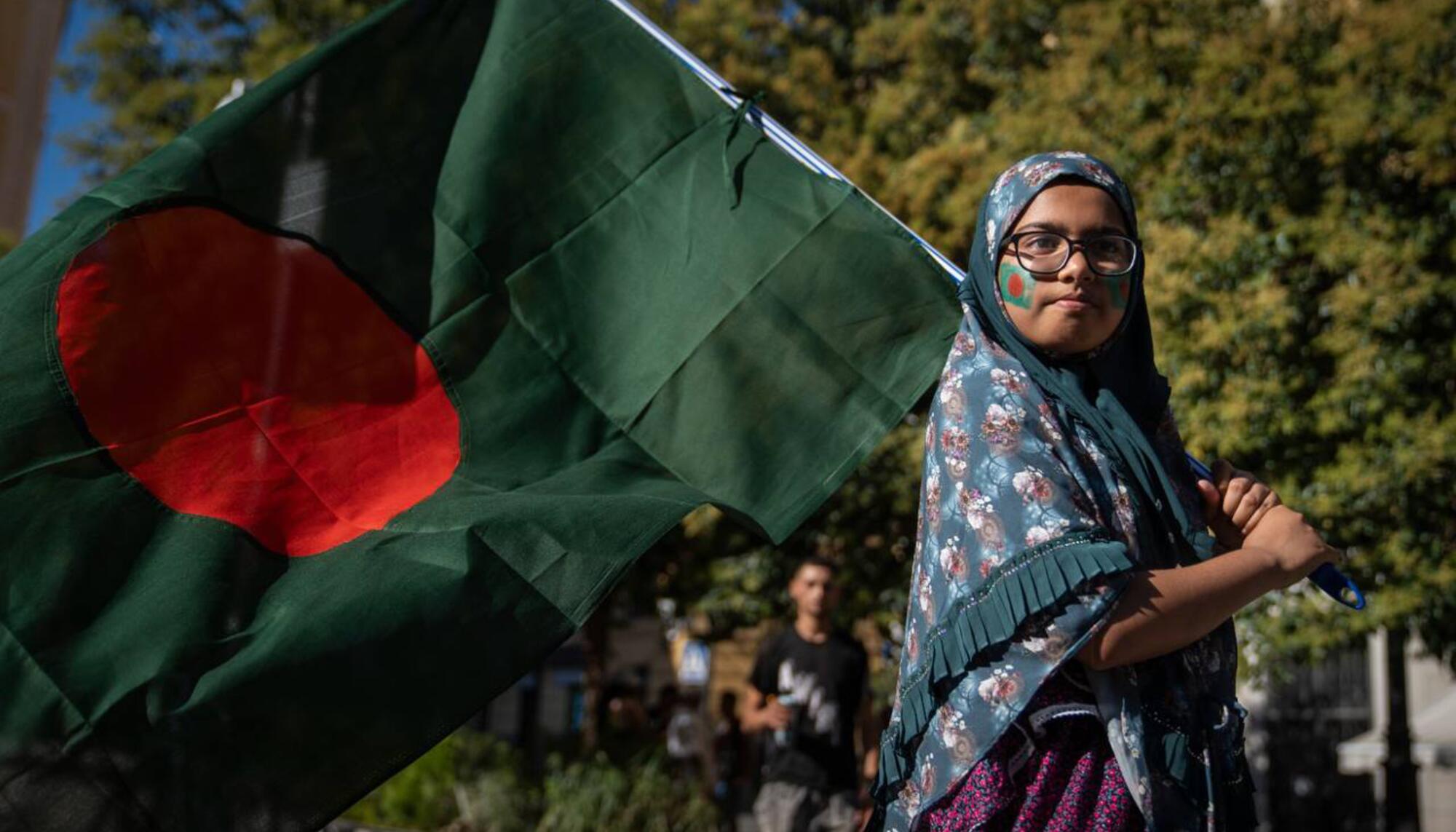 Una mujer de origen bangladesí con una bandera del país se manifiesta en Madrid para mostrar su respaldo a las protestas.