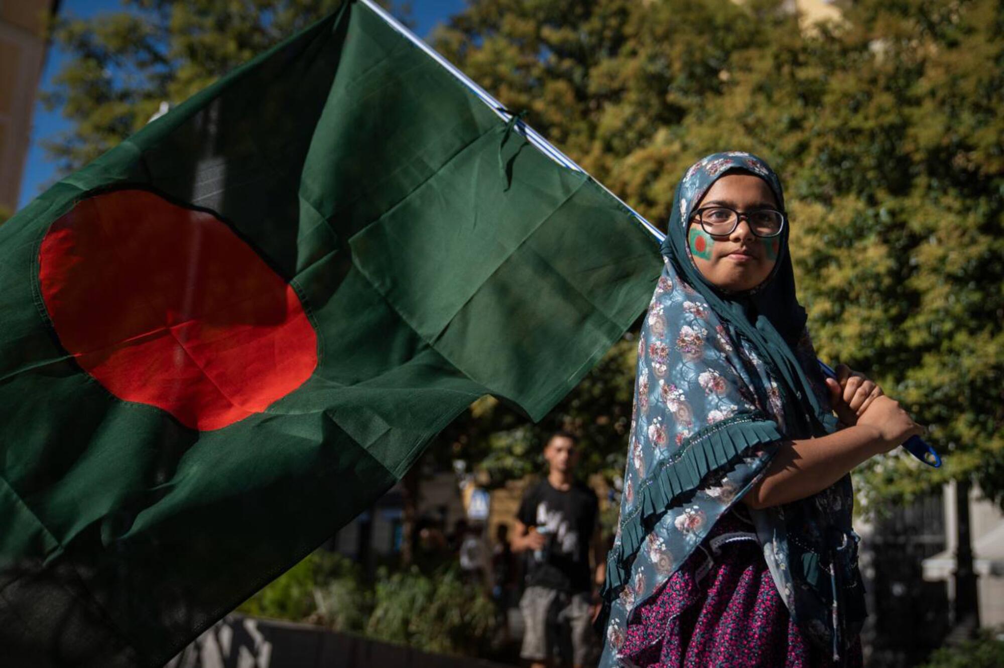 Una mujer de origen bangladesí con una bandera del país se manifiesta en Madrid para mostrar su respaldo a las protestas.